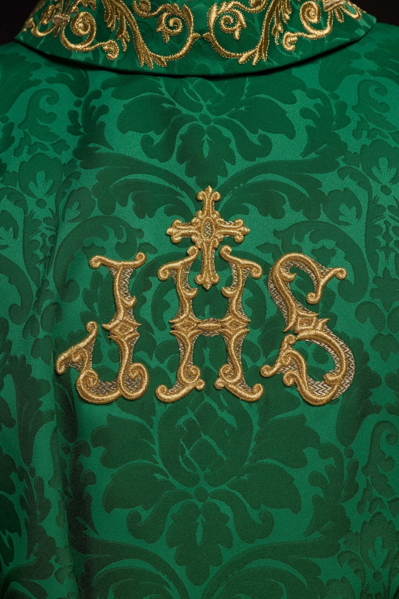 Casulla verde con motivo IHS y cuello ricamente bordado sobre tela decorativa